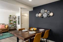 A bold black accent wall sets the tone in this dining space, where a solid wood table and gold-toned chairs create a warm, modern vibe for meals or game nights.