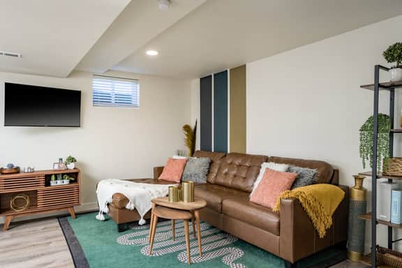 A cozy setup with a tufted leather couch, layered textures, and a mounted TV makes this space perfect for winding down after a day out in Denver.